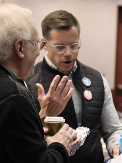 Gus and a volunteer are talking to get ready for a lobby day. They are reviewing the fact sheet for a bill together in the frame.