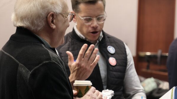 Gus and a volunteer are talking to get ready for a lobby day. They are reviewing the fact sheet for a bill together in the frame.