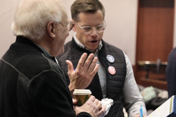 Gus and a volunteer are talking to get ready for a lobby day. They are reviewing the fact sheet for a bill together in the frame.