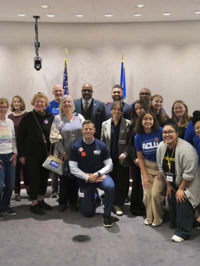 A group of staff, volunteers, and legislators in support of no-excuse absentee voting are standing in the Capitol, smiling at the camera.