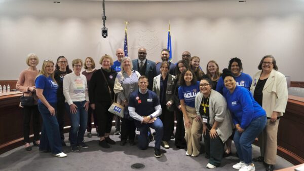 A group of staff, volunteers, and legislators in support of no-excuse absentee voting are standing in the Capitol, smiling at the camera.