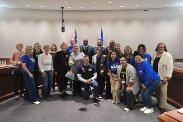 A group of staff, volunteers, and legislators in support of no-excuse absentee voting are standing in the Capitol, smiling at the camera.