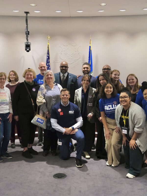 A group of staff, volunteers, and legislators in support of no-excuse absentee voting are standing in the Capitol, smiling at the camera.