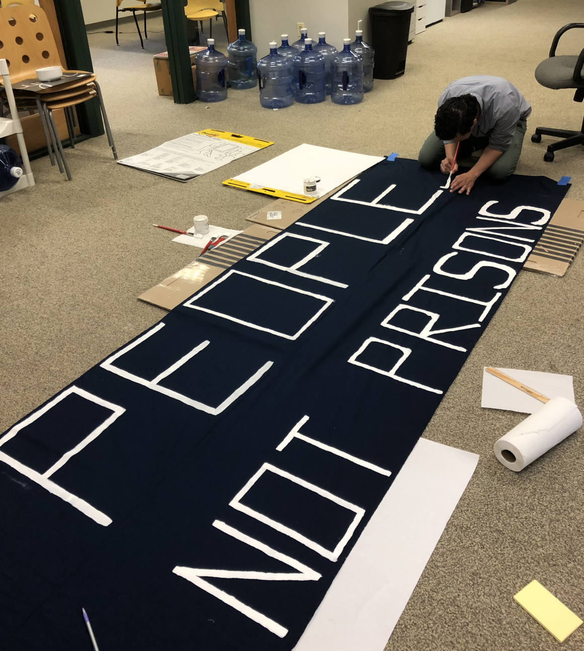 ACLU-CT staff member crouches with a paint brush over a banner that says "People Not Prisons"