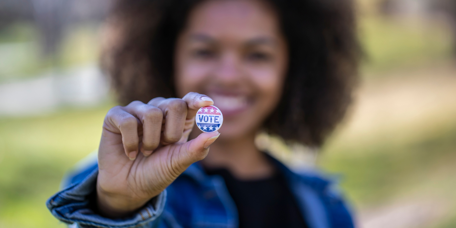 A black woman holding a button that reads "vote".