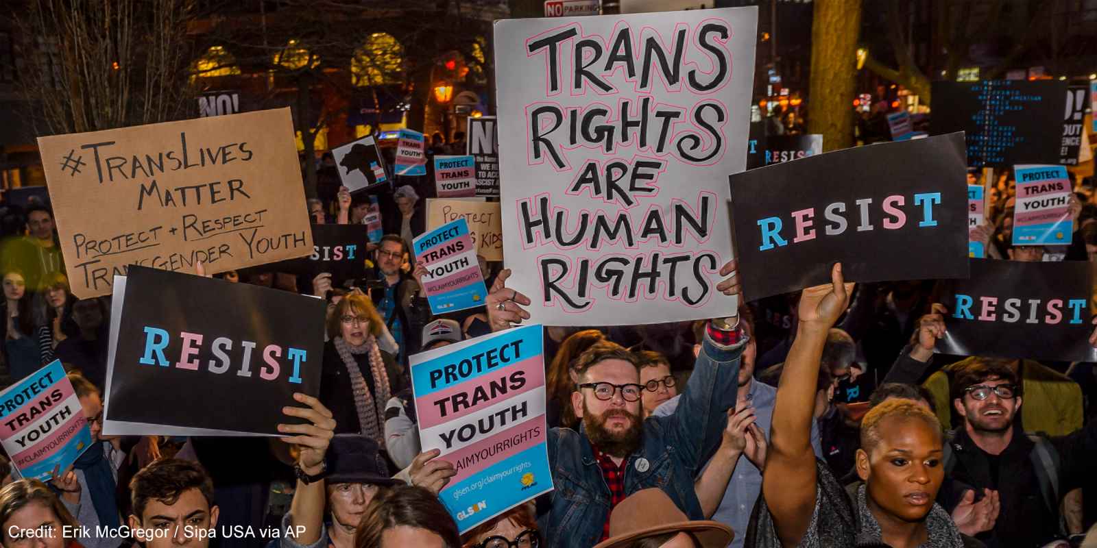 Protestors with signs advocating for the rights of trans youth.