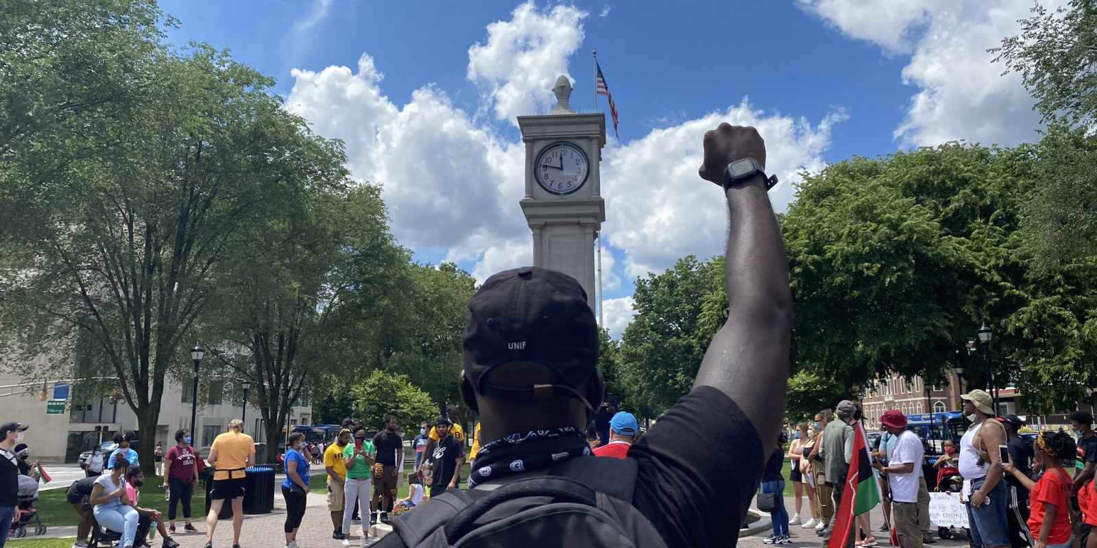 A Black man stands with his fist raised in the air.