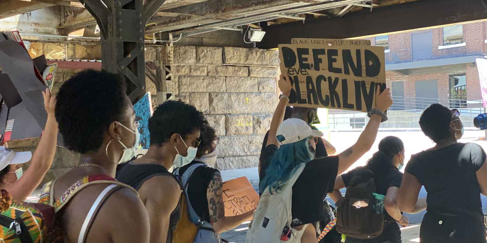 A group of protesters walks in Hartford. One holds a cardboard sign that says, in black letters, "defend Black lives"