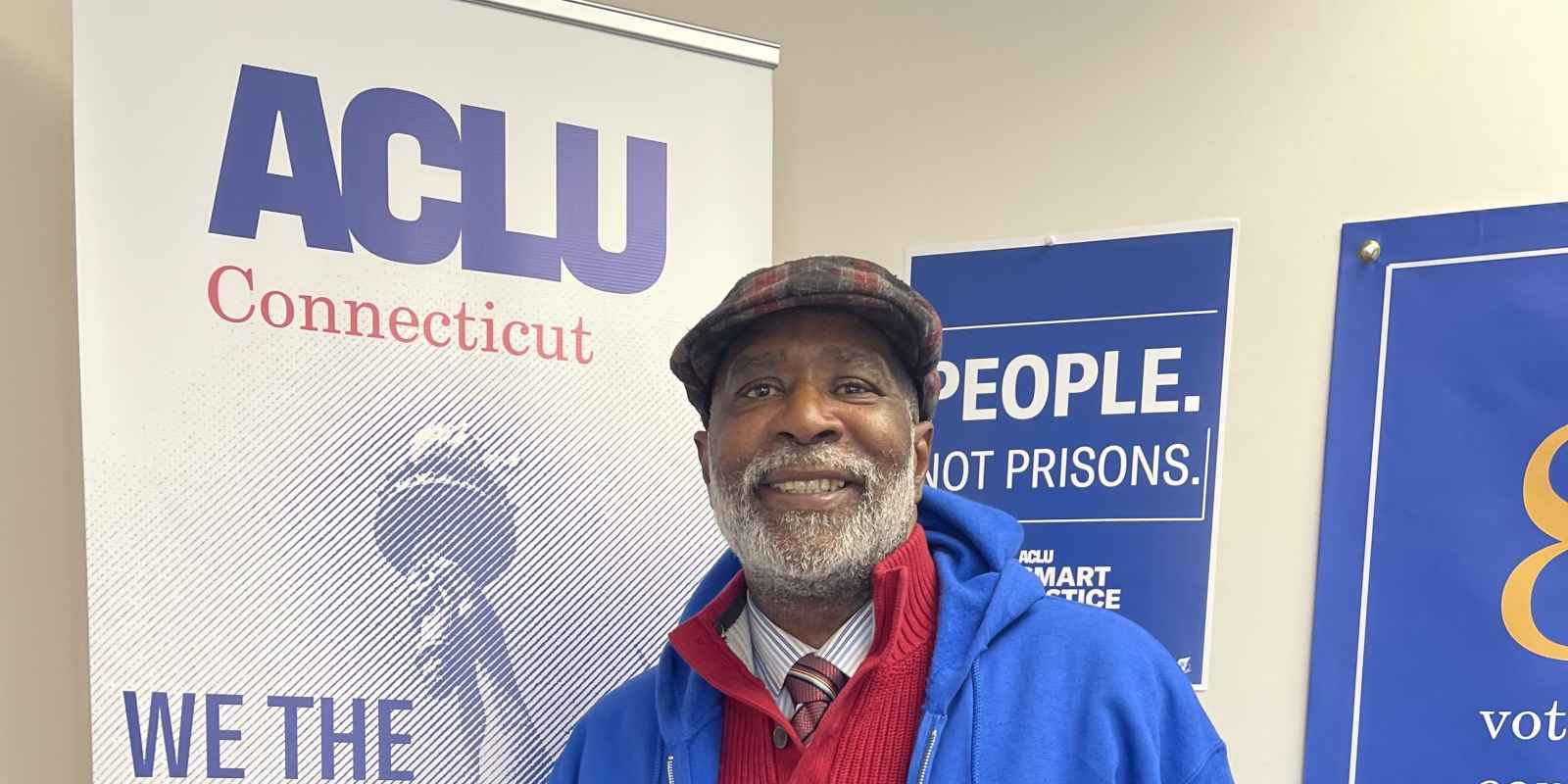 Smart Justice Leader Curtis Hudson standing and smiling next to an ACLU of CT poster