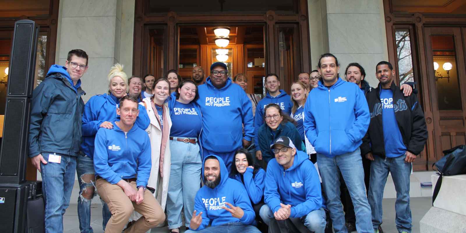 A group of approximately 20 people wearing ACLU bright blue t-shirts smiling at the camera, standing in front of the Capitol building in Hartford, Connecticut.