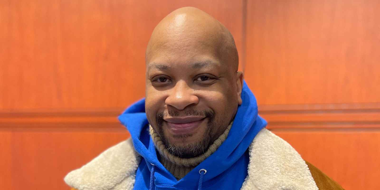 ACLU of CT smart justice leader Donald Rivers smiles, facing the camera and wearing a brown coat over a blue people not prisons hoodie