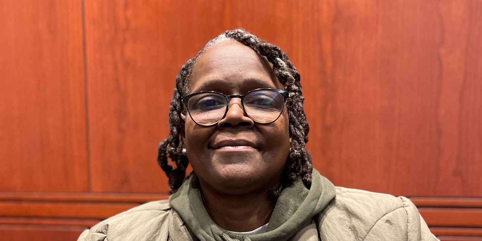 ACLU CT Smart Justice leader Terri Ricks sits, smiling at the camera and wearing a brown jacket and brown hoodie. 