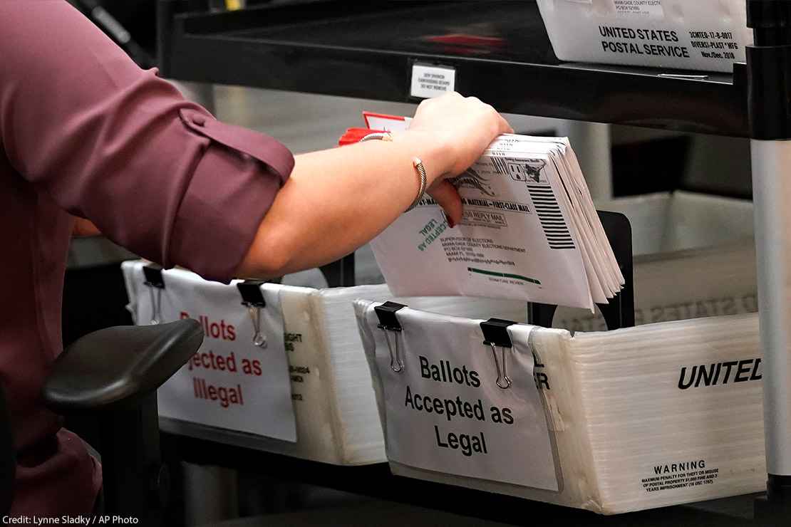 An election worker sorts vote-by-mail ballots in bins.