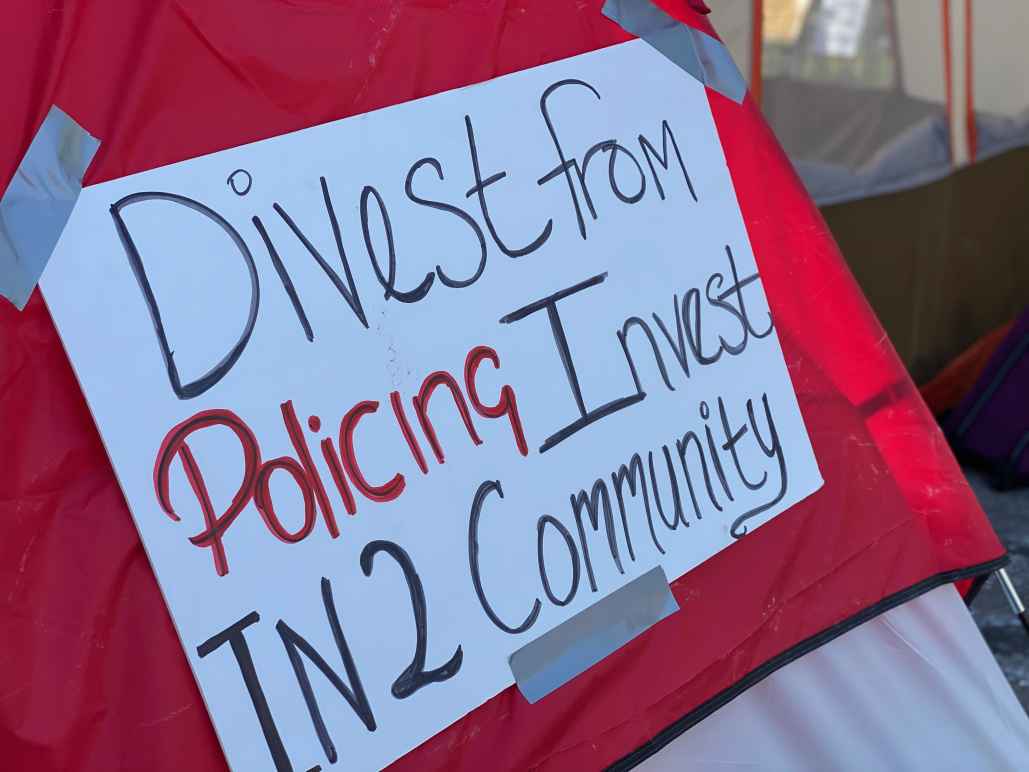 Red tent with white sign. Sign reads: Divest from policing / invest in2 community