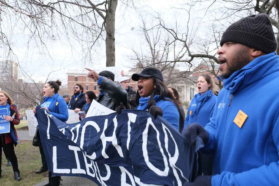 ACLU-CT Smart Justice leaders, in blue fleeces, stand side by side holding a "March for Liberation" banner. They are joining a chant.