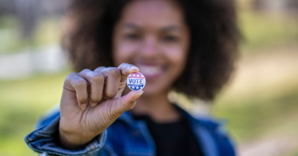 A black woman holding a button that reads "vote".