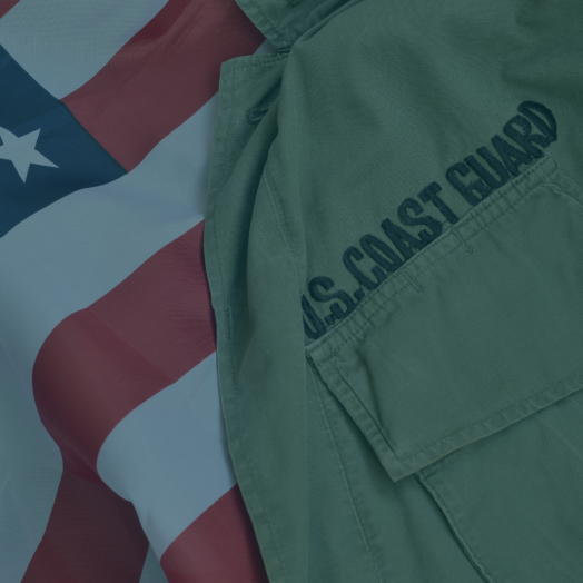 On the right, part of a U.S. Coast Guard uniform is visible, with "U.S. Coast Guard" stitching prominent. On the left and behind the uniform is the U.S.A. flag