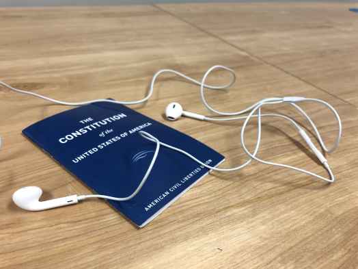 A blue Constitution of the United States, published by the ACLU, sits on a table under white headphones