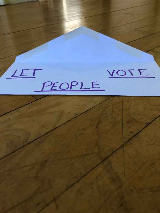 a white envelope against wood background. written on the envelope: LET PEOPLE VOTE