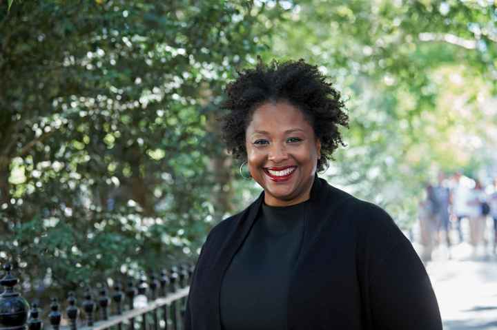 Deborah Archer, national ACLU president, is in the foreground. She is wearing a black shirt and blazer and is smiling, looking directly at the camera. Behind her is a leafy park. 