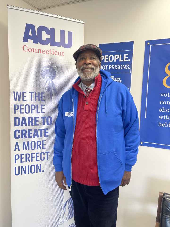 Smart Justice Leader Curtis Hudson standing and smiling next to an ACLU of CT poster