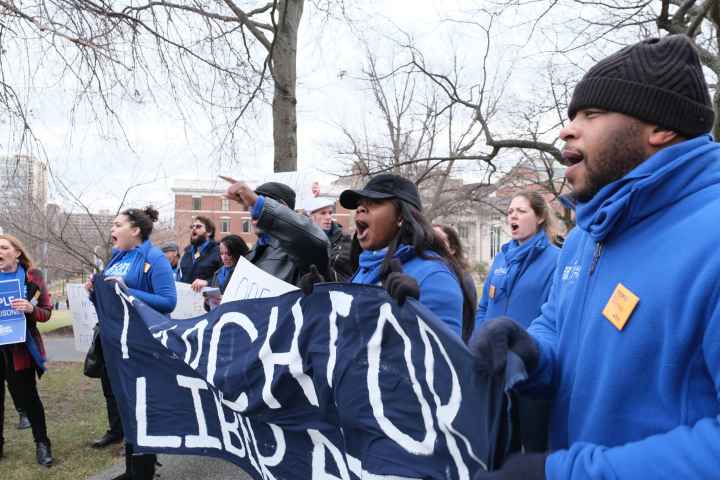 ACLU-CT Smart Justice leaders, in blue fleeces, stand side by side holding a "March for Liberation" banner. They are joining a chant.