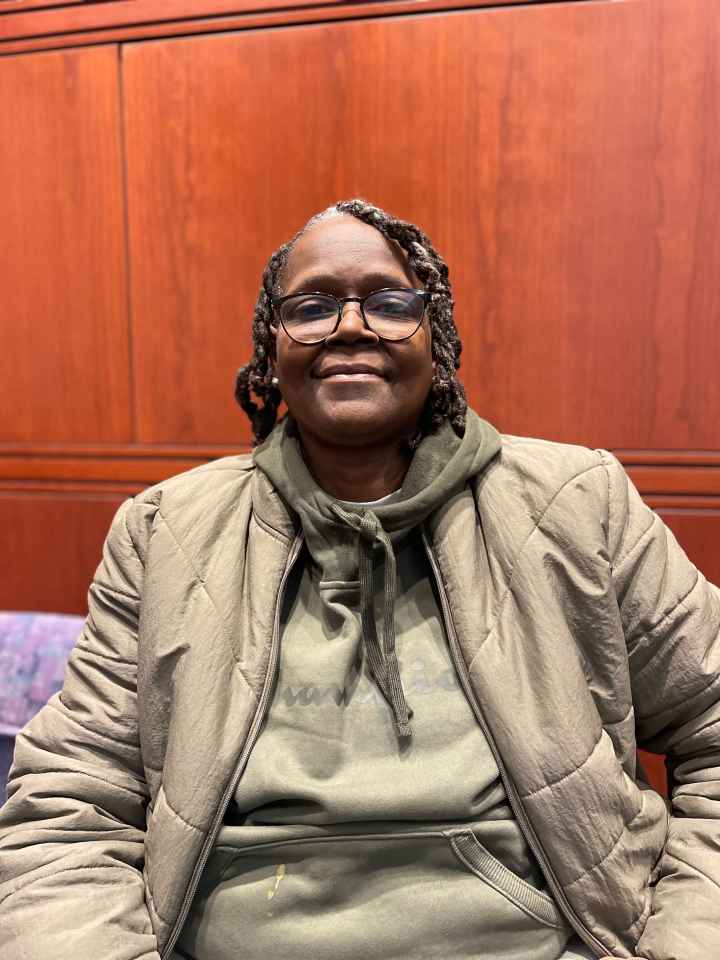 ACLU CT Smart Justice leader Terri Ricks sits, smiling at the camera and wearing a brown jacket and brown hoodie.