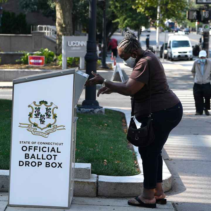 An Afrian-American woman drops a ballot into a State of Connecticut Official Ballot Drop Box outside Hartford City Hall.