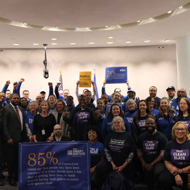 ACLU of Connecticut Smart Justice, CONECT, GHIAA, and Connecticut state legislators stand and sit in a group to support Clean Slate, behind a blue banner with a statistic about voters' support for Clean Slate ideas.