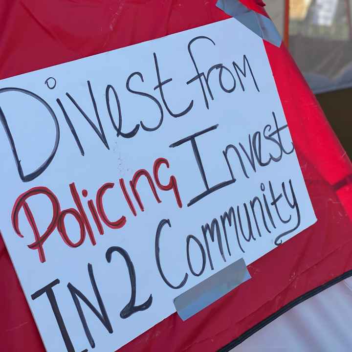 Red tent with white sign. Sign reads: Divest from policing / invest in2 community