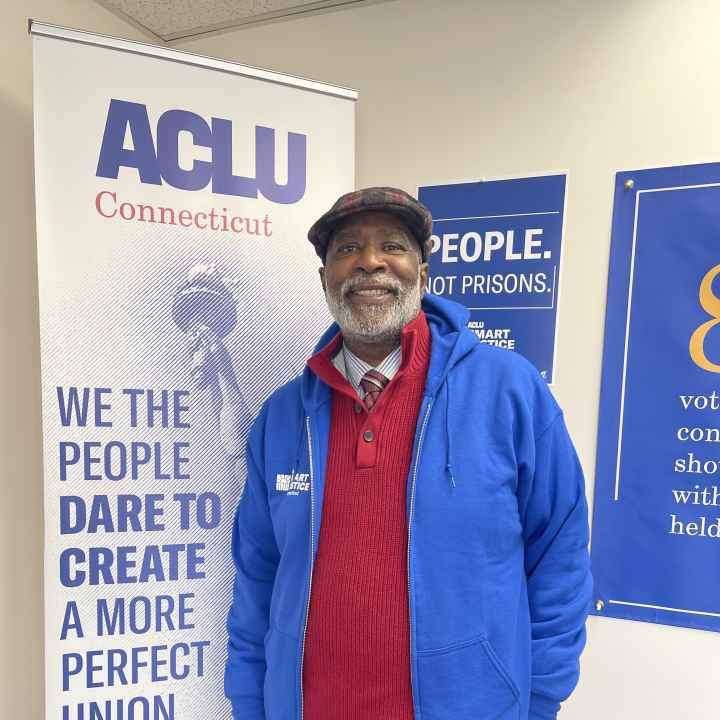 Smart Justice Leader Curtis Hudson standing and smiling next to an ACLU of CT poster