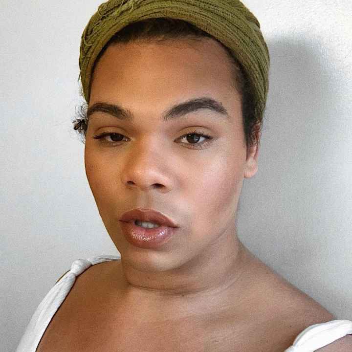 Erycka Ortiz, ACLU of Connecticut field organizer, stands facing the camera. She is wearing a green head wrap and a white top, and she is looking straight at the camera.