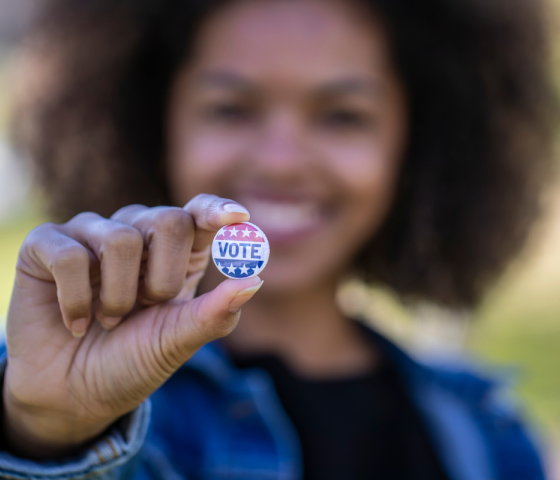 A black woman holding a button that reads "vote".