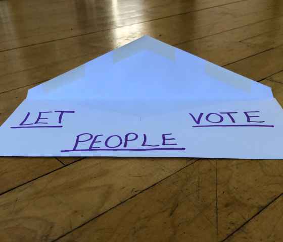 a white envelope against wood background. written on the envelope: LET PEOPLE VOTE