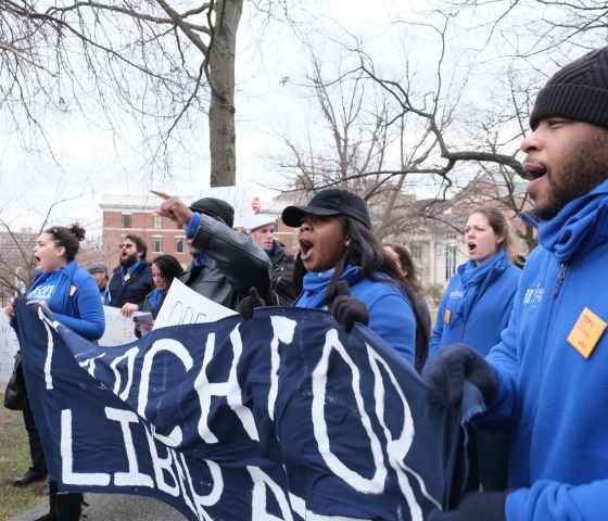 ACLU-CT Smart Justice leaders, in blue fleeces, stand side by side holding a "March for Liberation" banner. They are joining a chant.